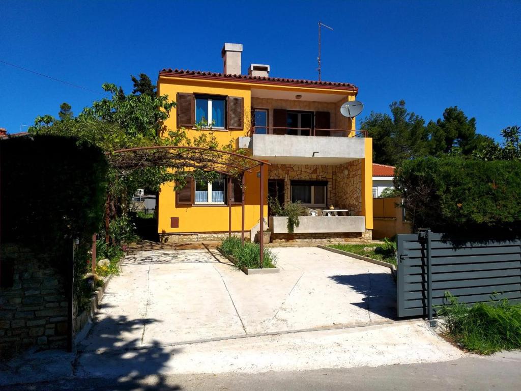 ein gelbes Haus mit einer Einfahrt davor in der Unterkunft Appartements Clementina in Premantura