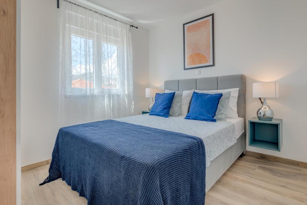 a bedroom with a bed with blue pillows and a window at Apartman Bonaca in Trogir