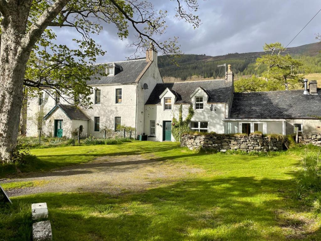 uma grande casa branca com uma parede de pedra em Inverlael Farm Cottages em Inverlael