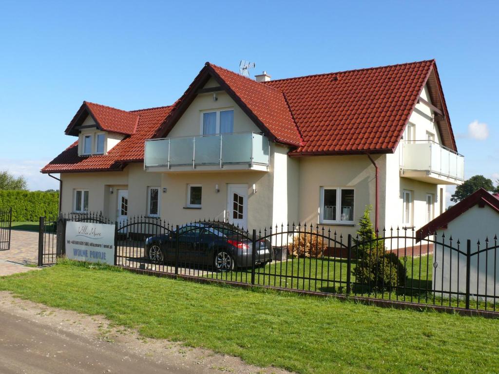 una casa blanca con techo rojo y valla negra en Juvenka, en Dziwnówek