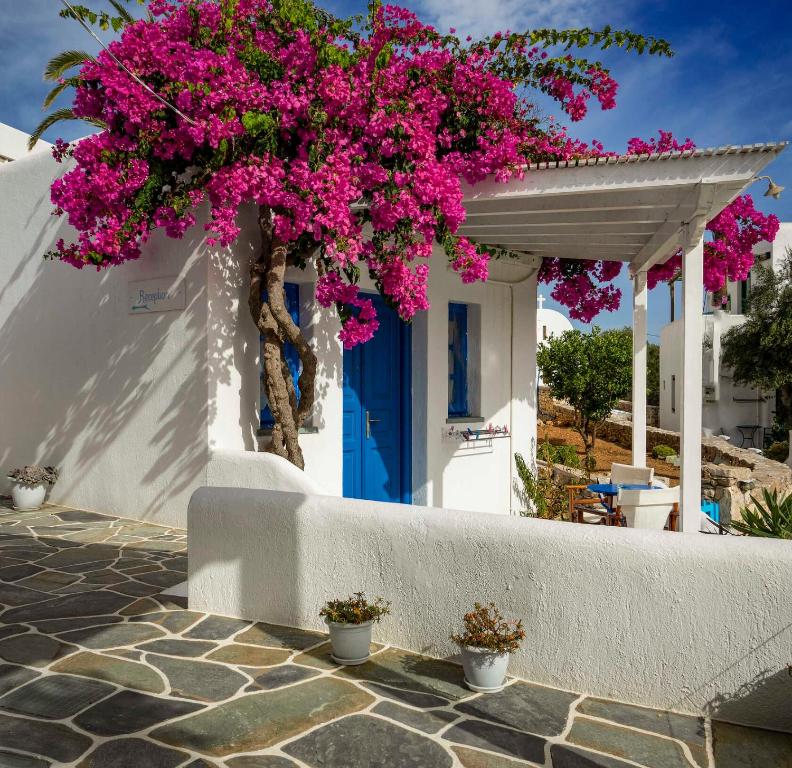 una casa blanca con una puerta azul y flores rosas en Meltemi en Chora Folegandros