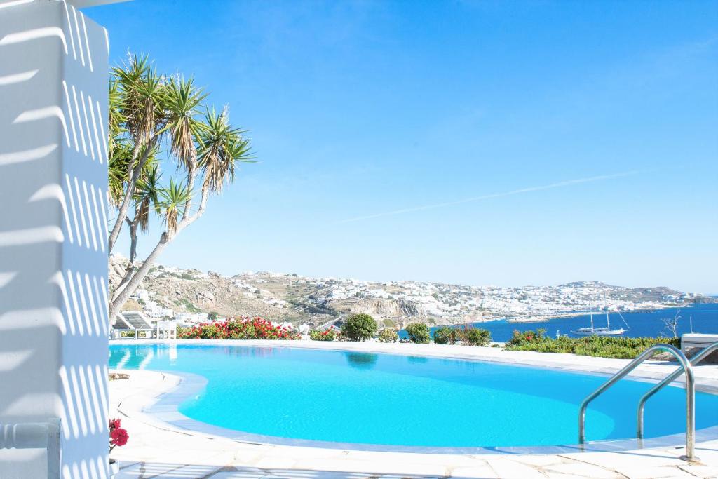 a swimming pool with palm trees and the ocean at Adikri Villas & Suites in Tourlos