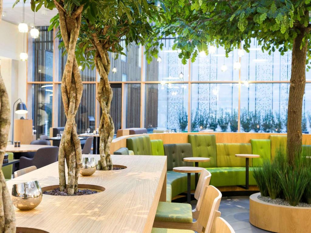 einen Tisch in einem Restaurant mit Bäumen und Stühlen in der Unterkunft Novotel Amsterdam Schiphol Airport in Hoofddorp