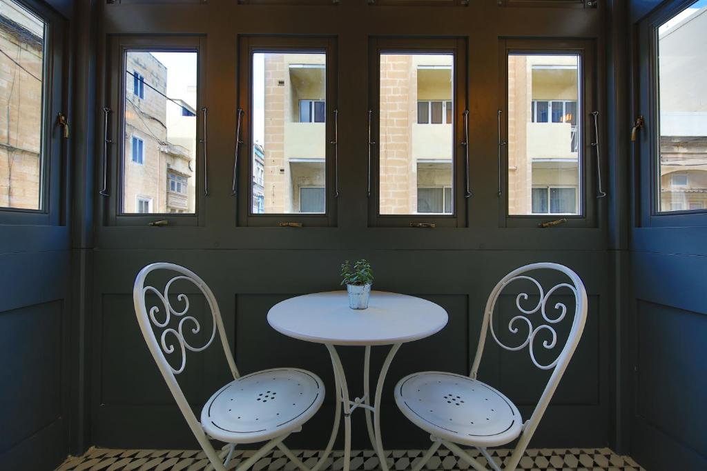 a table and two chairs in a room with windows at Lady Todd in Sliema