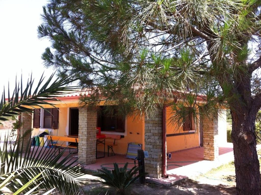 una pequeña casa amarilla con patio y árbol en Villa Oasi dei Fenicotteri, en Porto Pino