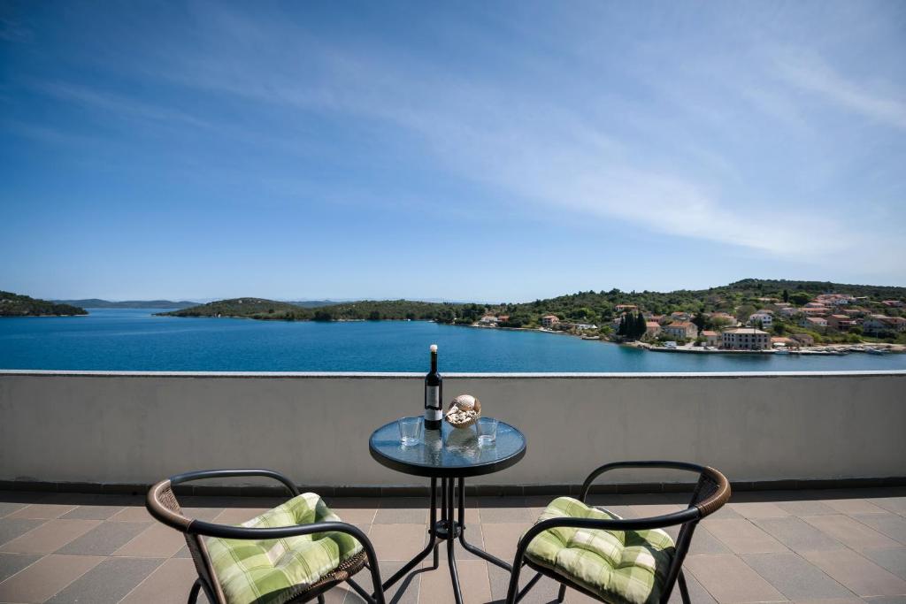 un tavolo in vetro con 2 sedie e una bottiglia di vino sul balcone di Picić Guesthouse a Luka