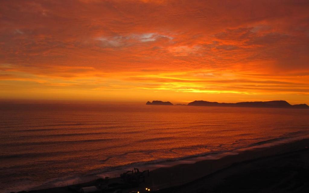 un coucher de soleil sur l'océan et des montagnes en arrière-plan dans l'établissement Blue Coast Lima Private Rooms, à Lima