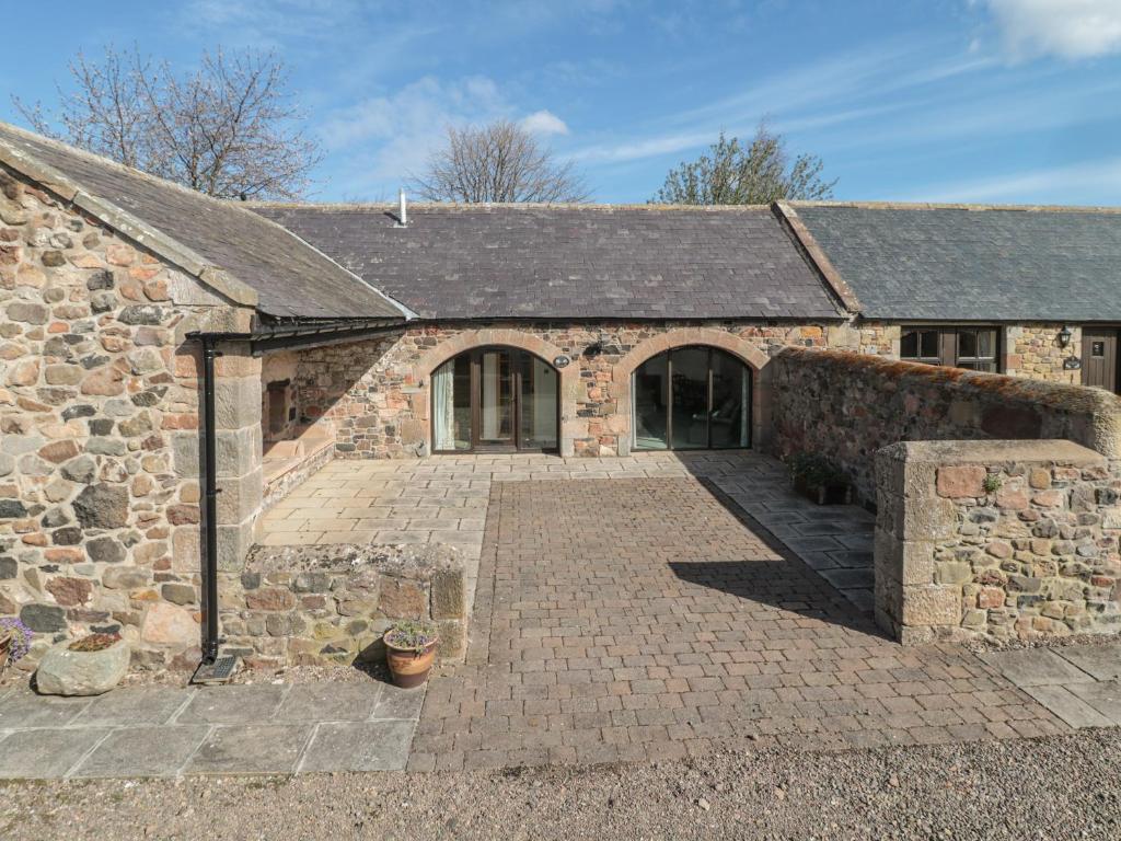 an old stone building with a brick driveway at Lupin Cottage in Wooler