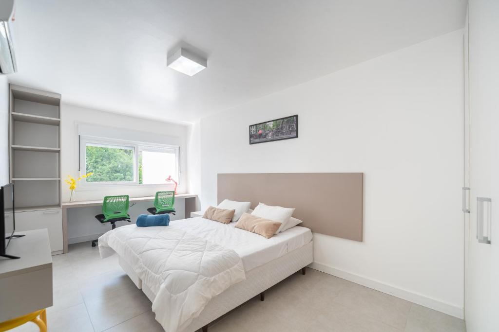 a white bedroom with a bed and a green chair at Apartamento impecável Fernando Machado 828 in Porto Alegre