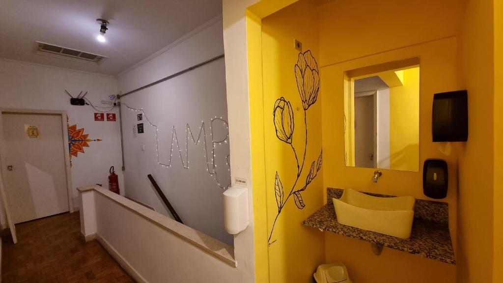 La salle de bains est pourvue d'un mur jaune, d'un lavabo et d'un miroir. dans l'établissement Lamparina Hostel, à São Paulo