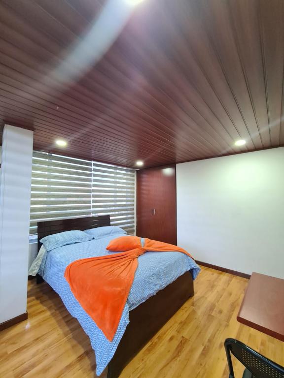 a bedroom with a large bed with an orange blanket at Hotel Casa Huesped Kiwi in Bogotá