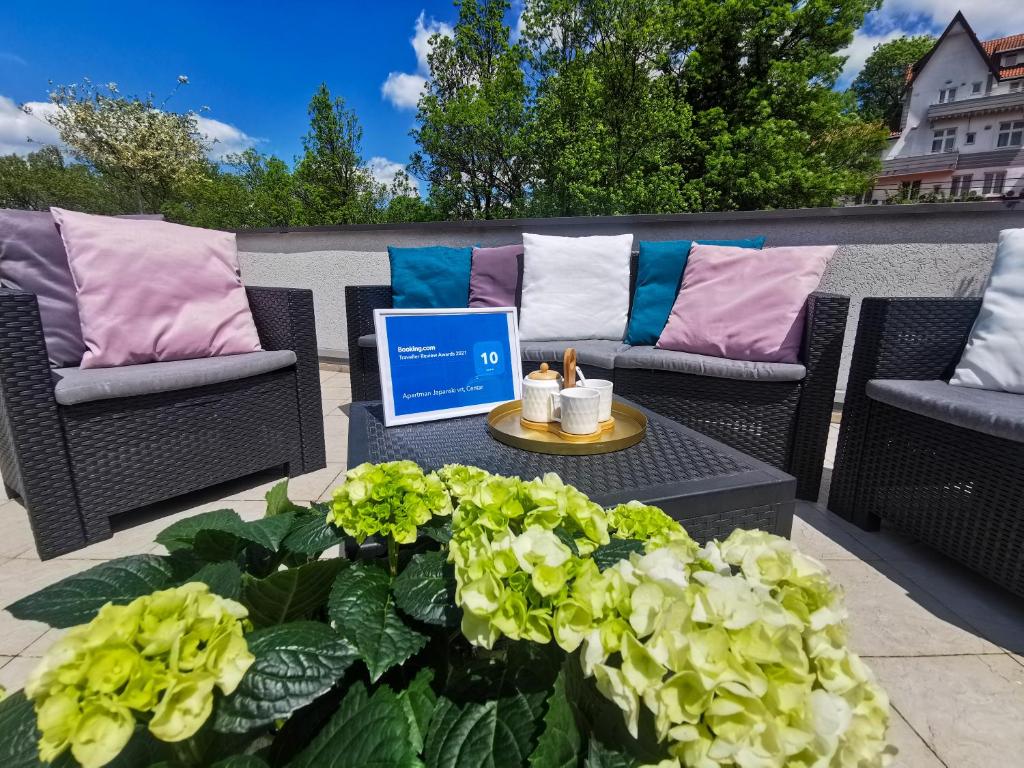 a patio with two wicker chairs and a table and flowers at Apartman Japanski vrt, Centar in Vrnjačka Banja
