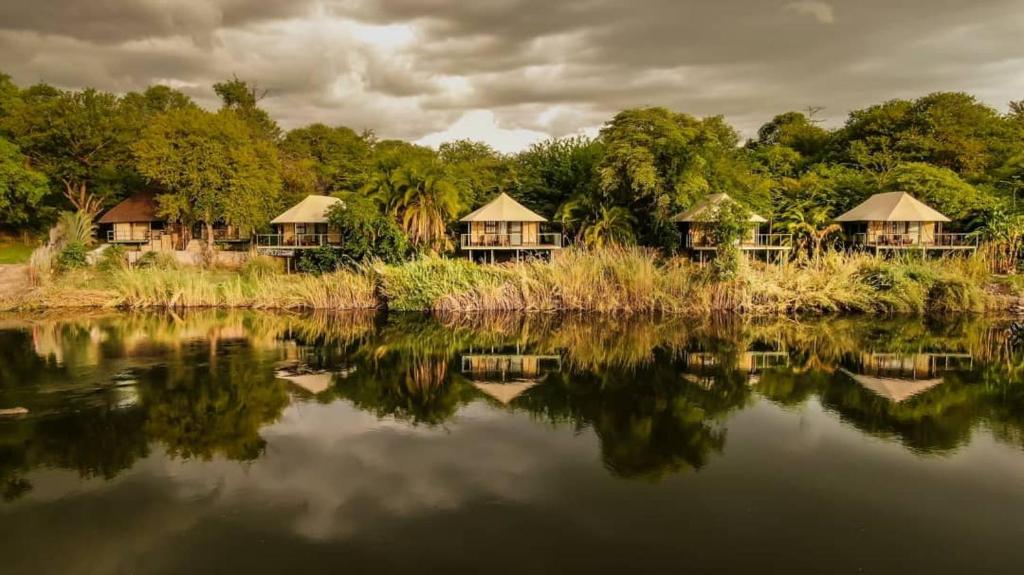 Shametu River Lodge في Divundu: مجموعة اكواخ بجانب جسم ماء
