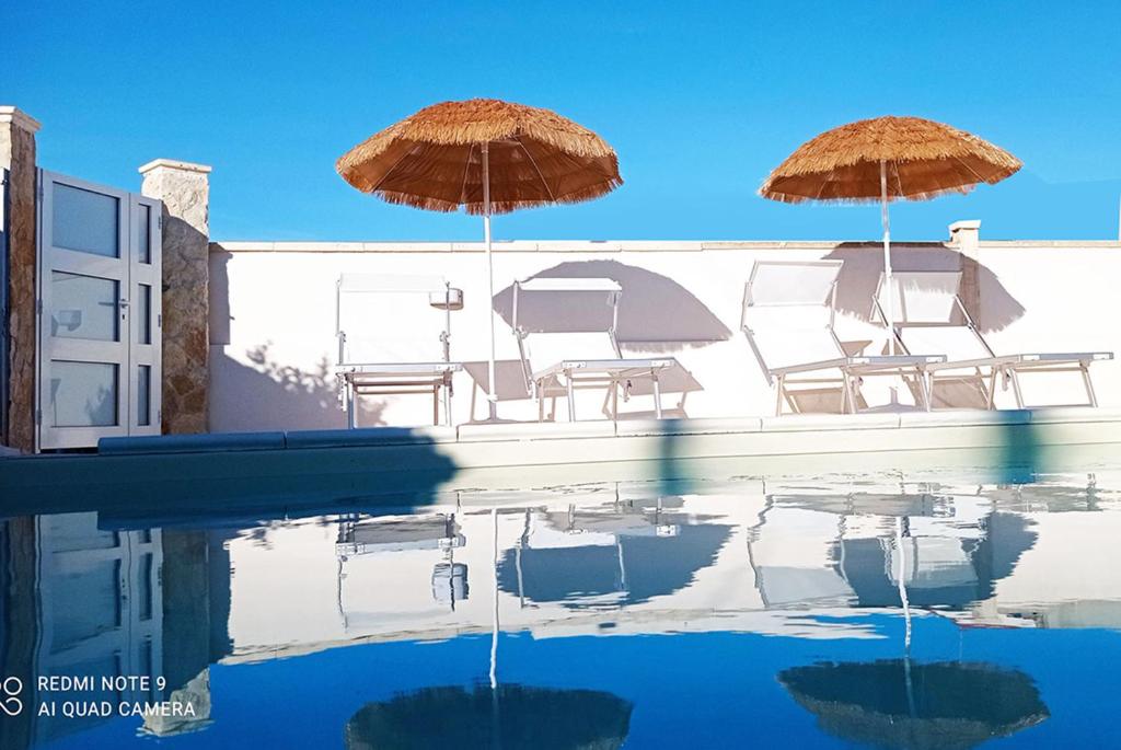 un gruppo di sedie e ombrelloni accanto alla piscina di I Gufi Bed & Breakfast Marzamemi a Marzamemi