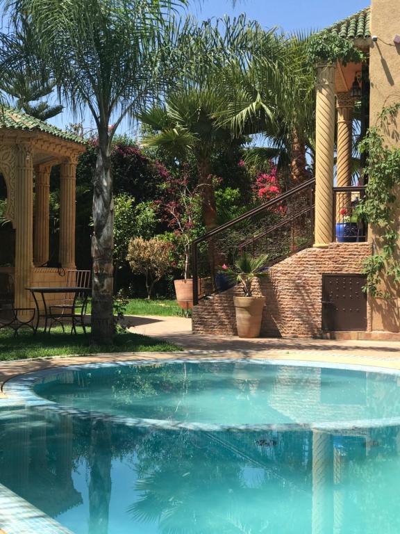 a swimming pool in front of a house with palm trees at Les Jardins de Ryad Bahia in Meknès