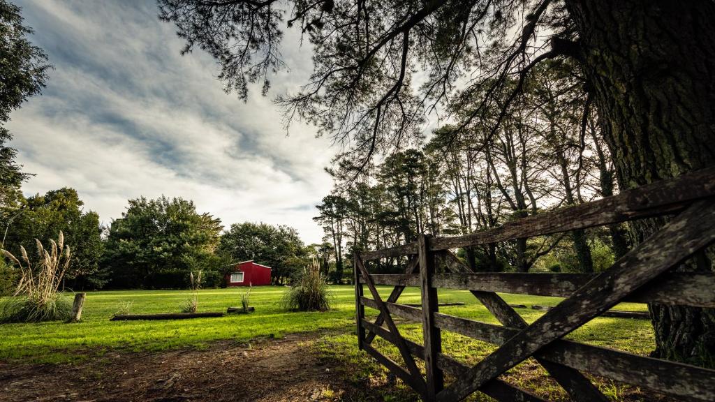 a wooden fence in a field with a red barn at NomeolvidesMás in Tandil