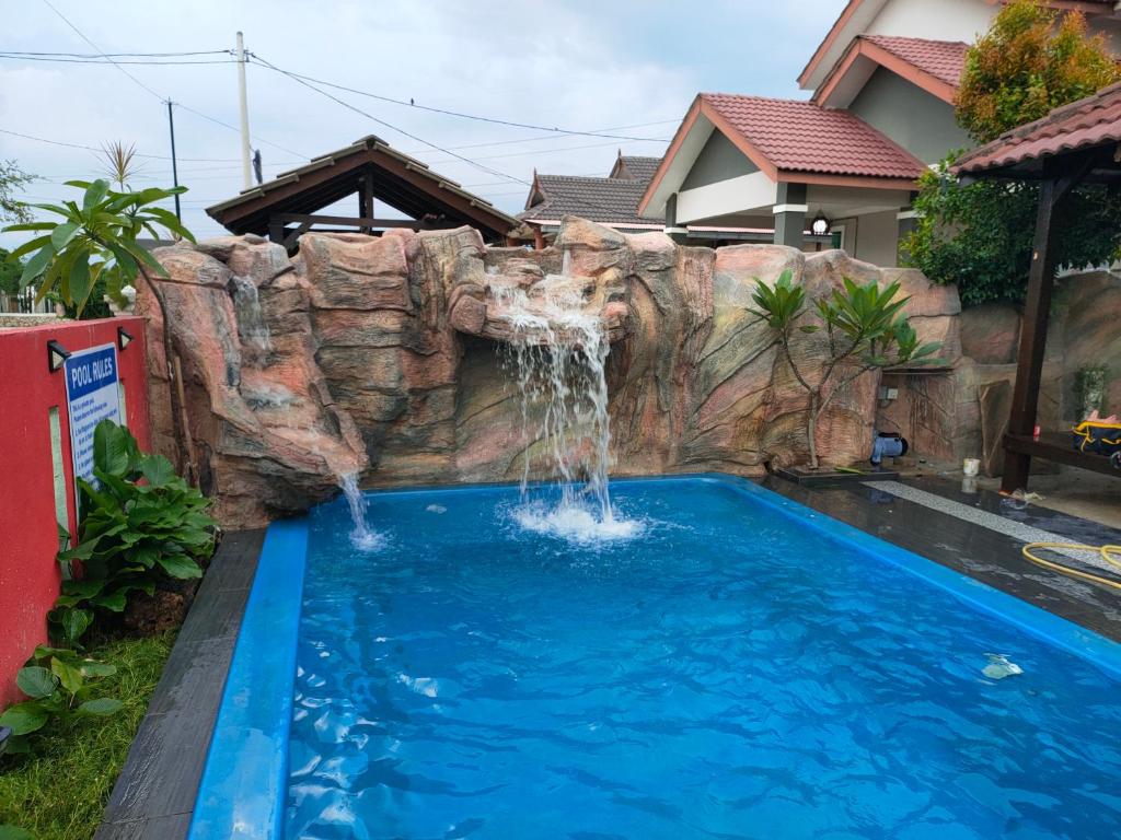 a swimming pool with a waterfall in front of a house at Roemahkoe Holidayhome in Malacca