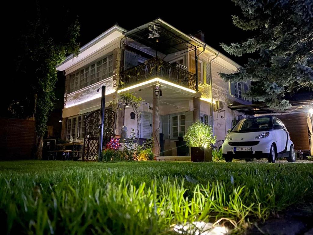 een witte auto geparkeerd voor een huis 's nachts bij Garden Budha Relax Apartman, parking, BBQ, terrace in Siófok