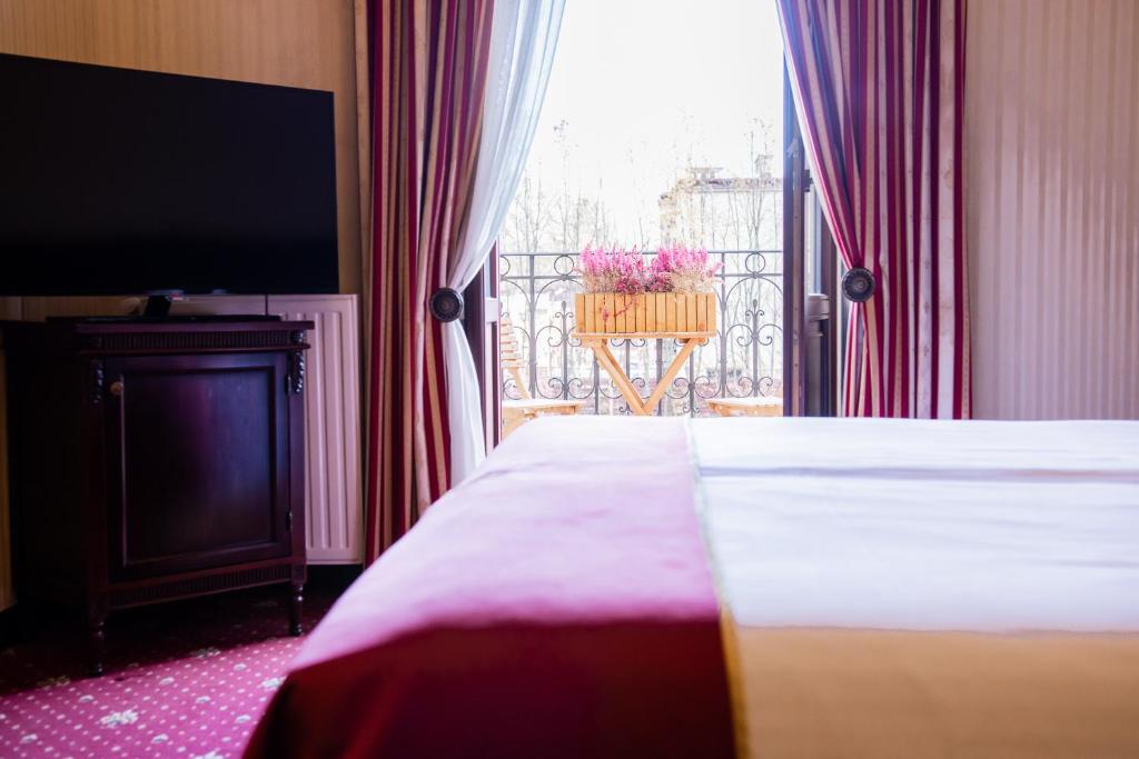 Hotel bed foreground with TV and open balcony door showing wooden flower box outside