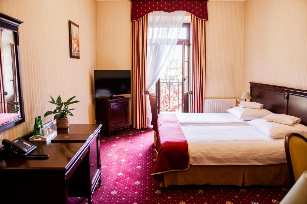 Bright hotel bedroom with twin beds, red accents, wooden desk, TV and open balcony door.