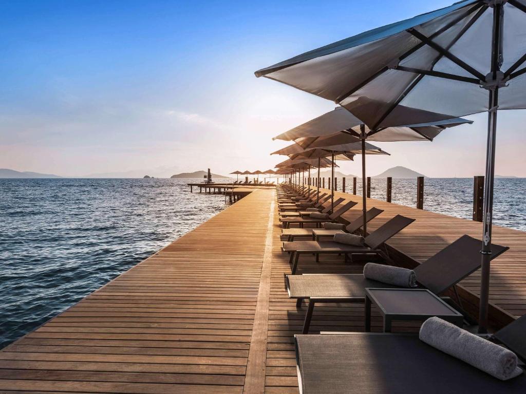 ein langer Pier mit Stühlen und Sonnenschirmen auf dem Wasser in der Unterkunft Swissôtel Resort Bodrum Beach in Turgutreis