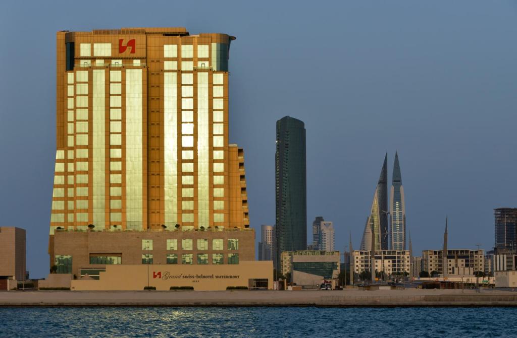 Grand Swiss-Belhotel Waterfront Seef في المنامة: أفق المدينة مع المباني الصفراء الطويلة والمياه