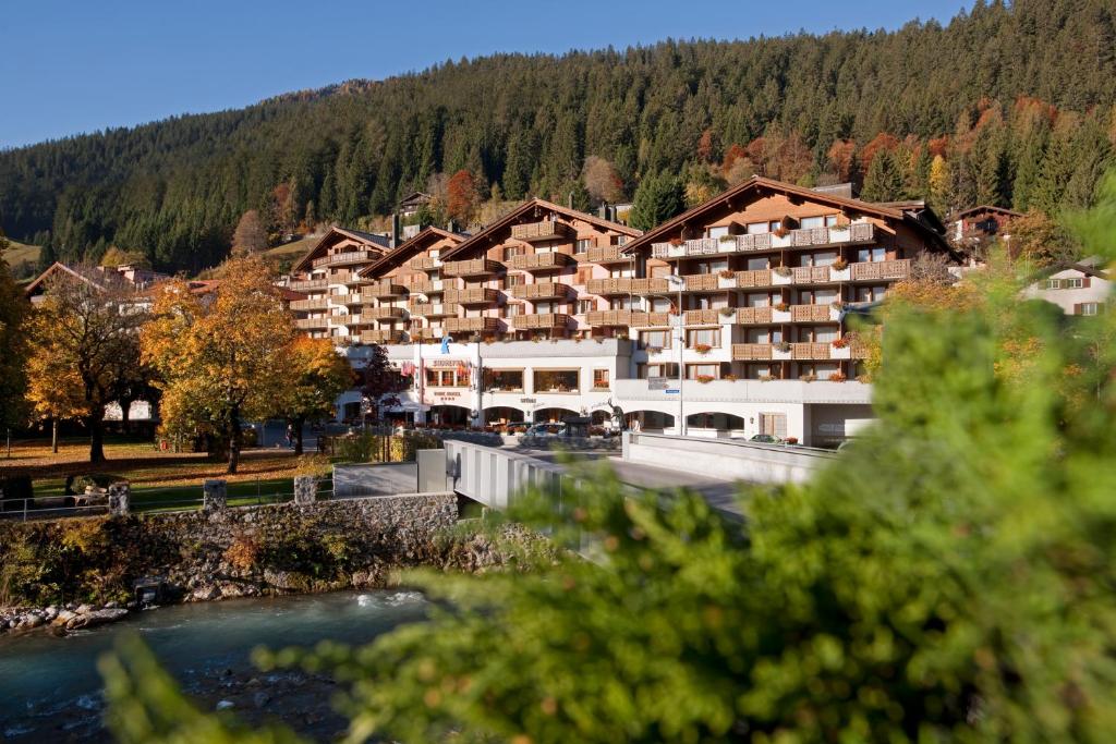 een hotel in de bergen met een rivier en bomen bij Silvretta Parkhotel in Klosters
