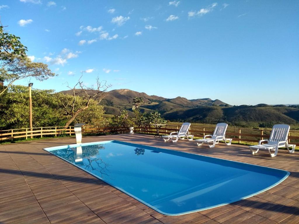 a swimming pool with chairs and a deck with mountains in the background at Pousada Capão Fôrro in São Roque de Minas