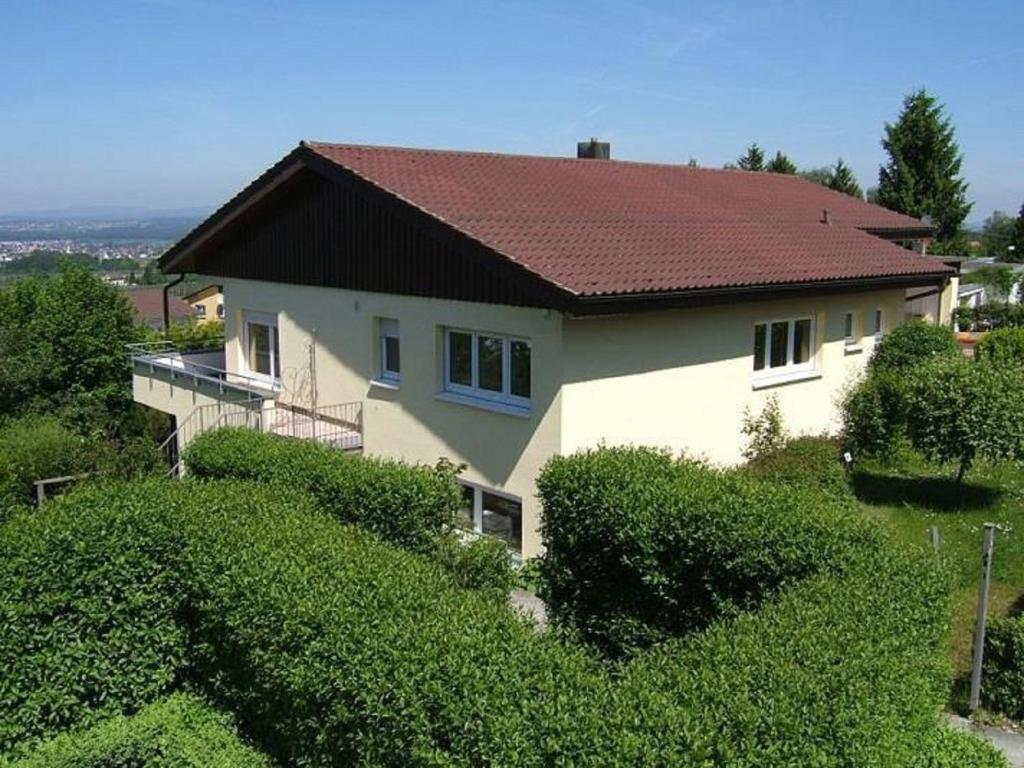 a white house with a red roof and bushes at Ferienwohnung Stryck in Tettnang