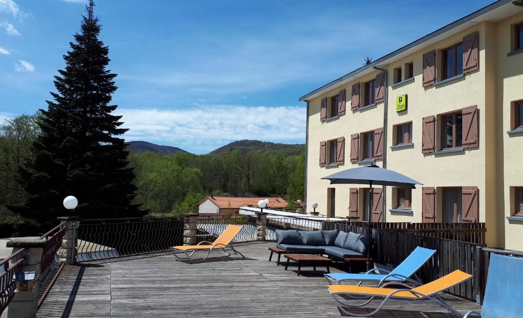 a patio with chairs and an umbrella and a building at Logis La Rose Des Vents in Volvic