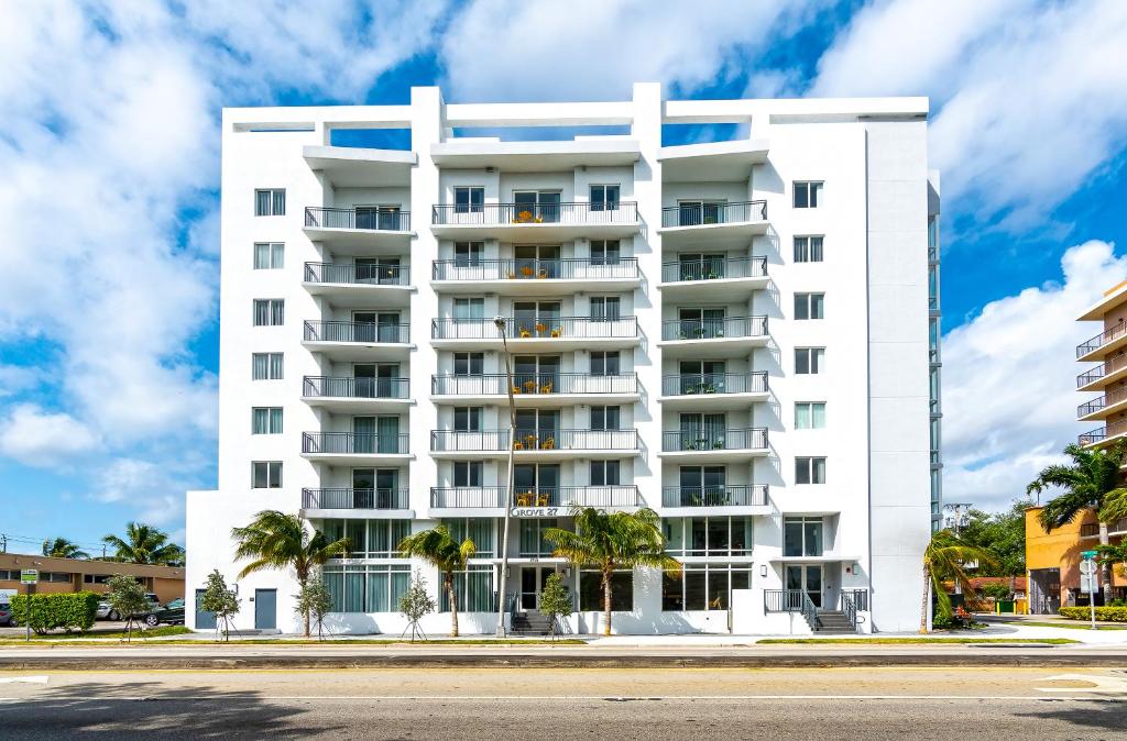 a white building with palm trees in front of it at Roami at Grove 27 in Miami