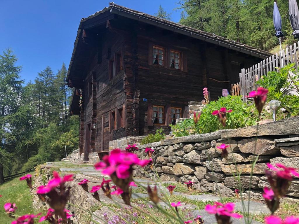 a log cabin with pink flowers in front of it at Atelier Berg zum Bildji in Staldenried