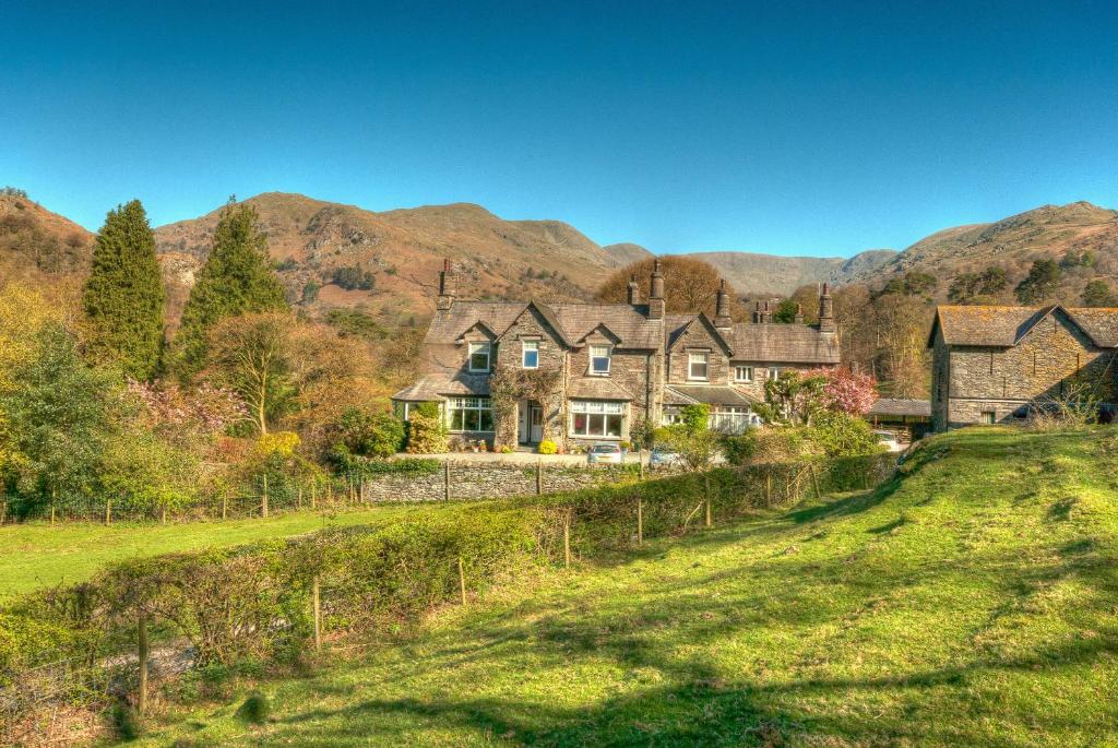 a large house on a hill with mountains in the background at Crow How Country Guest House in Ambleside