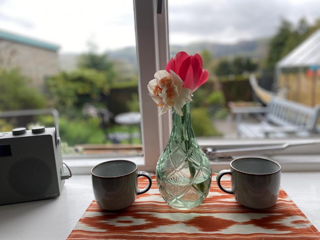 a vase with flowers and two cups on a table at The Paddle Nook in Pitlochry
