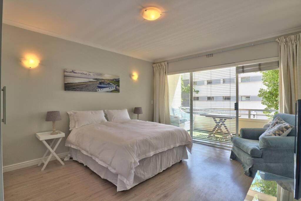 a bedroom with a bed and a chair and a window at Clifton 1st Beach Studio in Cape Town