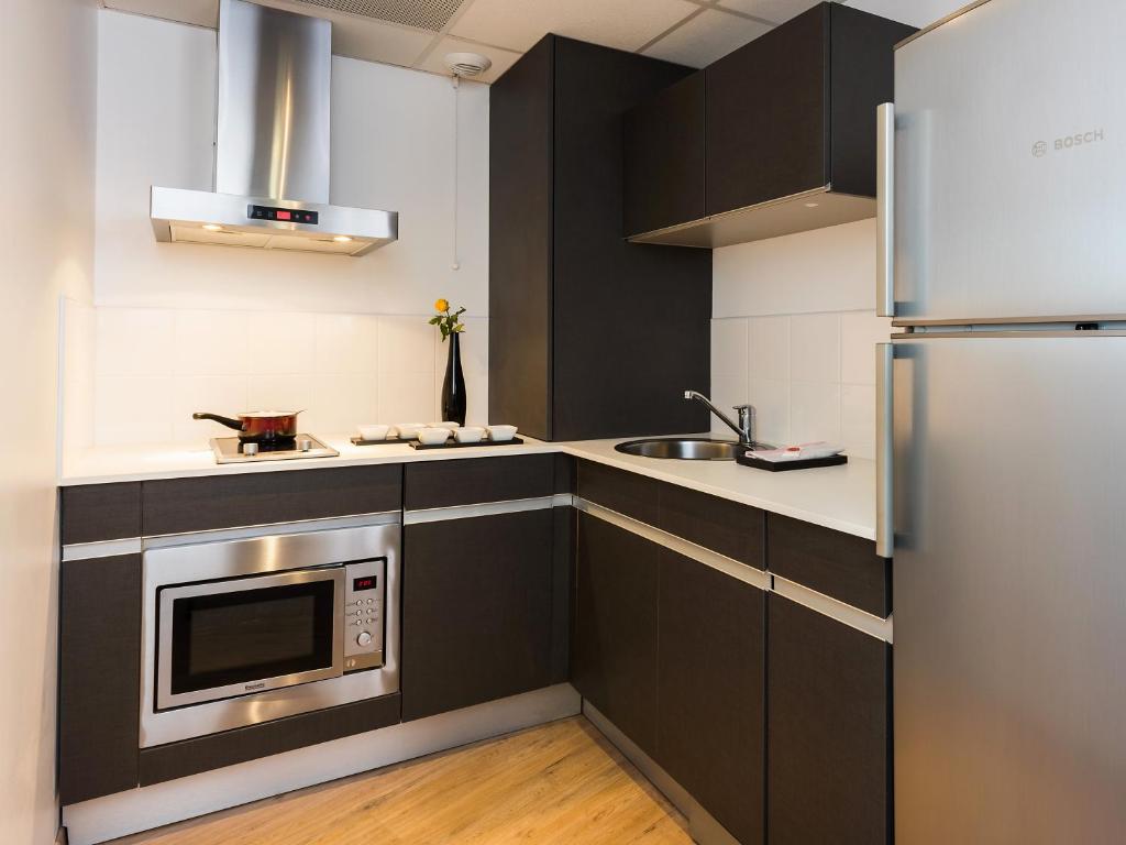 a kitchen with black cabinets and a stainless steel refrigerator at Ténéo Apparthotel Talence Arthena in Talence