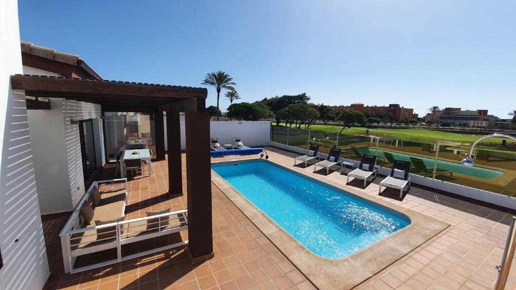a swimming pool with lounge chairs next to a building at Villa BELLA on Golf in La Estancia, Caleta Fuste-Fuerteventura in Caleta De Fuste