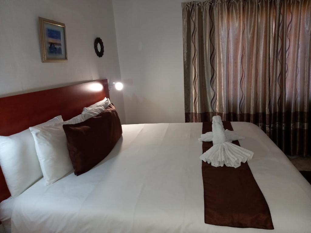 um quarto com uma cama grande com lençóis brancos e almofadas castanhas em Rest Shade Bed and Breakfast em Palapye