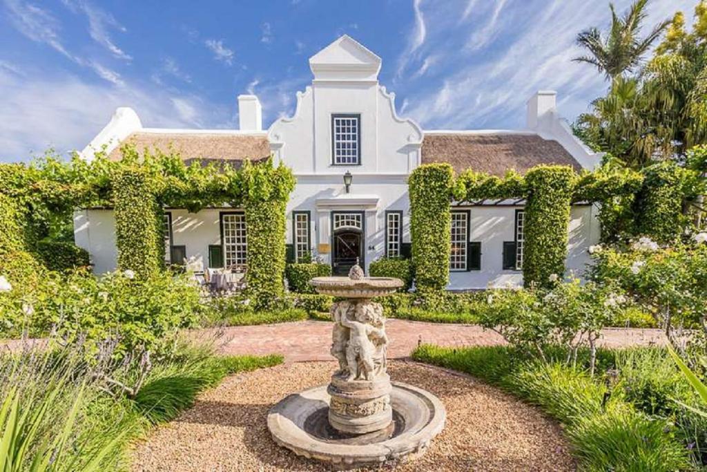 ein großes weißes Haus mit einem Brunnen davor in der Unterkunft Van der Stel Manor in Stellenbosch