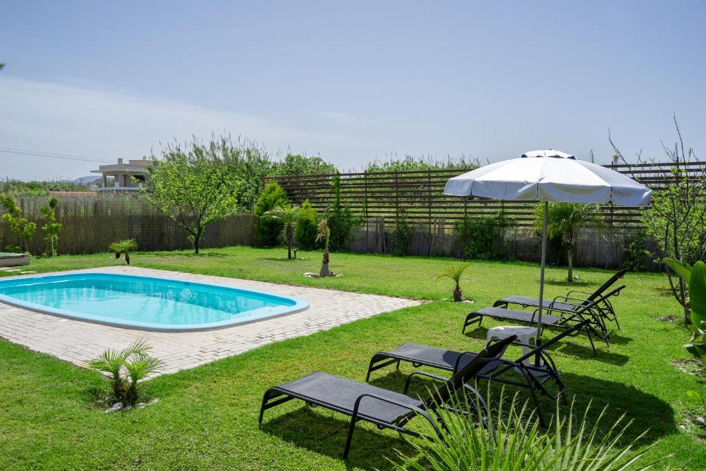 a yard with a pool with chairs and an umbrella at M&B Luxury House in Theologos