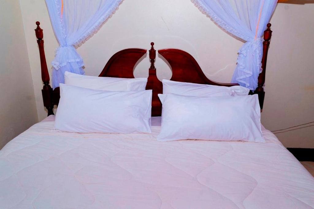 Cama blanca con almohadas blancas y cortinas azules en Kijungu Hill Hotel Hoima, en Hoima