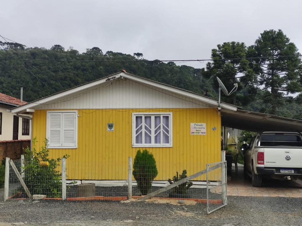 a yellow house with a car parked in front of it at pousada alternativa dora in Urubici