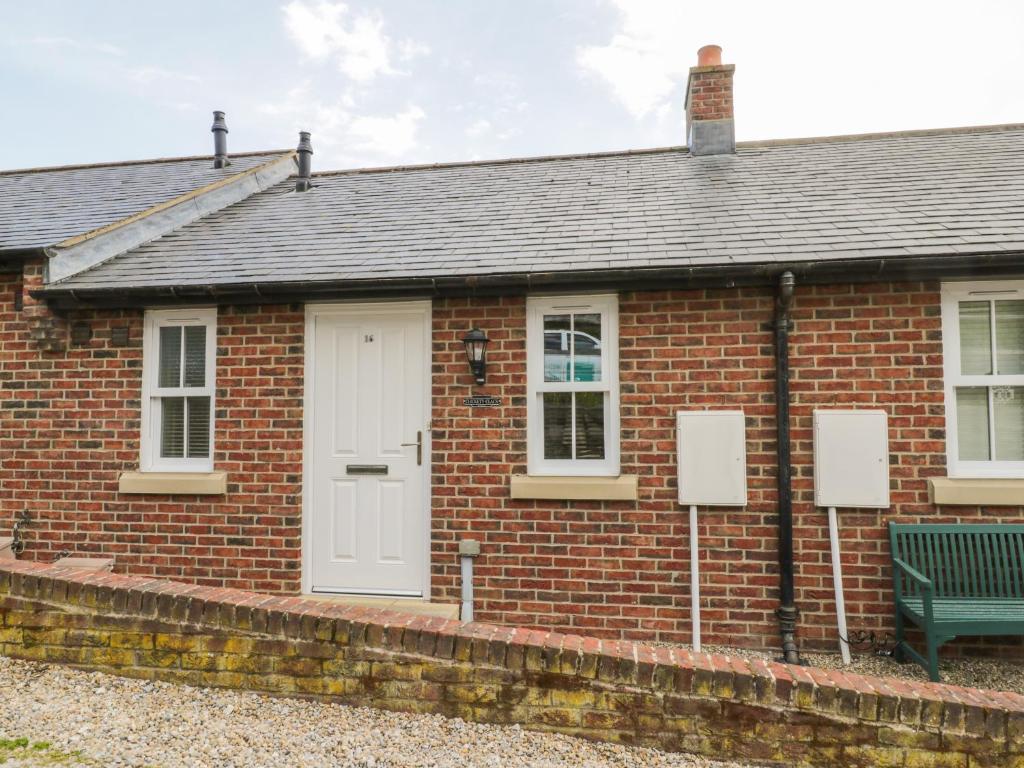 una casa de ladrillo rojo con una puerta blanca y un banco en Clickety-Clack Cottage en Whitby