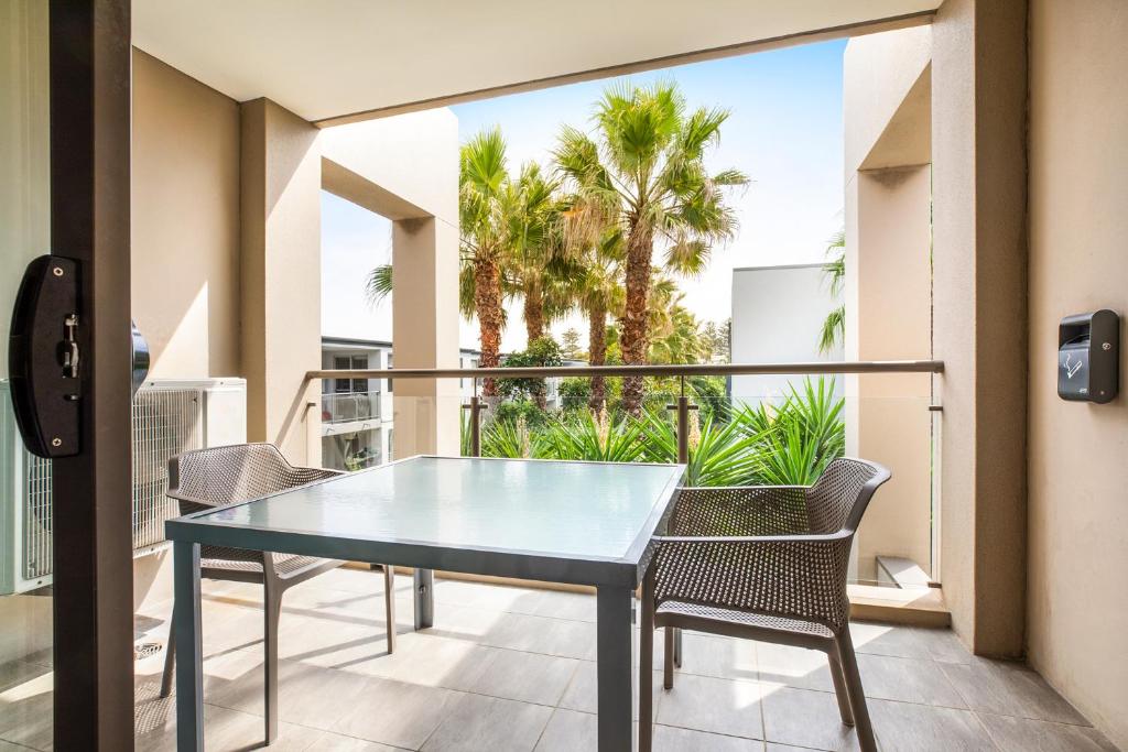 a table and chairs on a balcony with palm trees at Narrabeen Sands Hotel by Nightcap Plus in Narrabeen