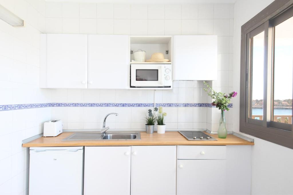 a white kitchen with a sink and a microwave at Aparthotel Niu d´Aus in Portopetro