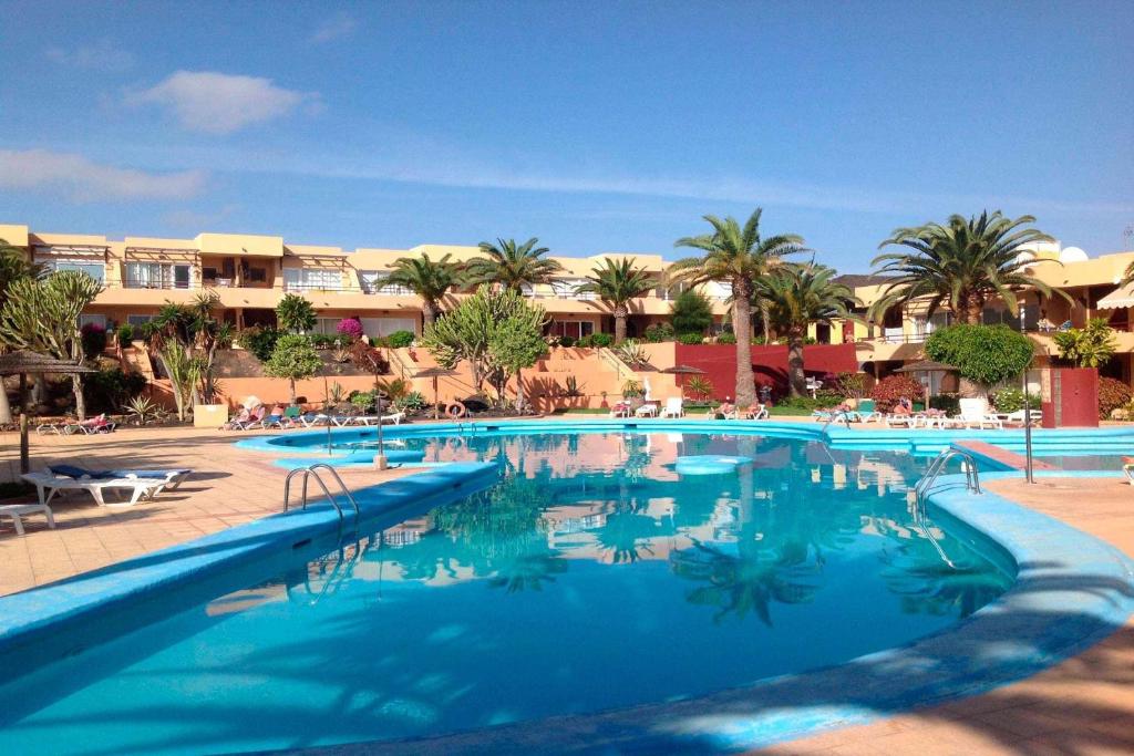 a pool at a resort with palm trees and buildings at Apartamento Kalma by Vacanzy Collection in Corralejo