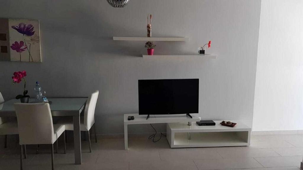 uma sala de estar com televisão e uma mesa com cadeiras em Apartamento Perseo em Corralejo