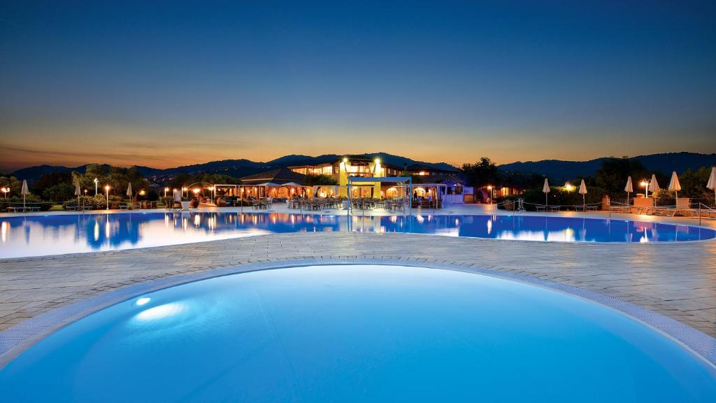 een groot zwembad in een resort 's nachts bij Hotel Baia Del Porto in Budoni