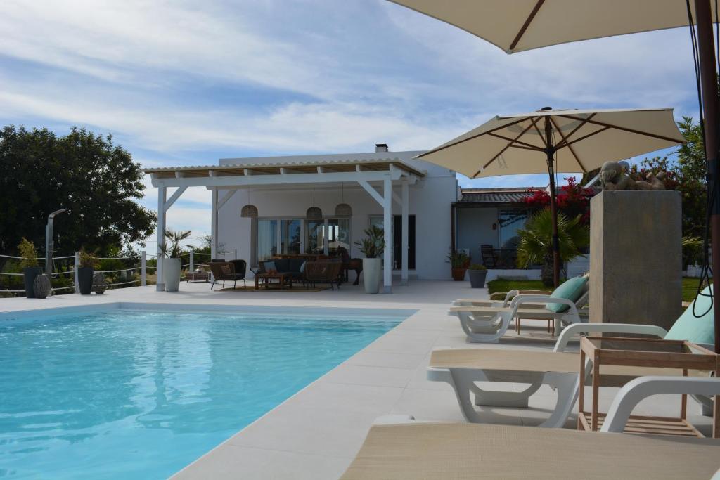 uma piscina com cadeiras e um guarda-sol ao lado de uma casa em Quinta Luz do Sol em Moncarapacho