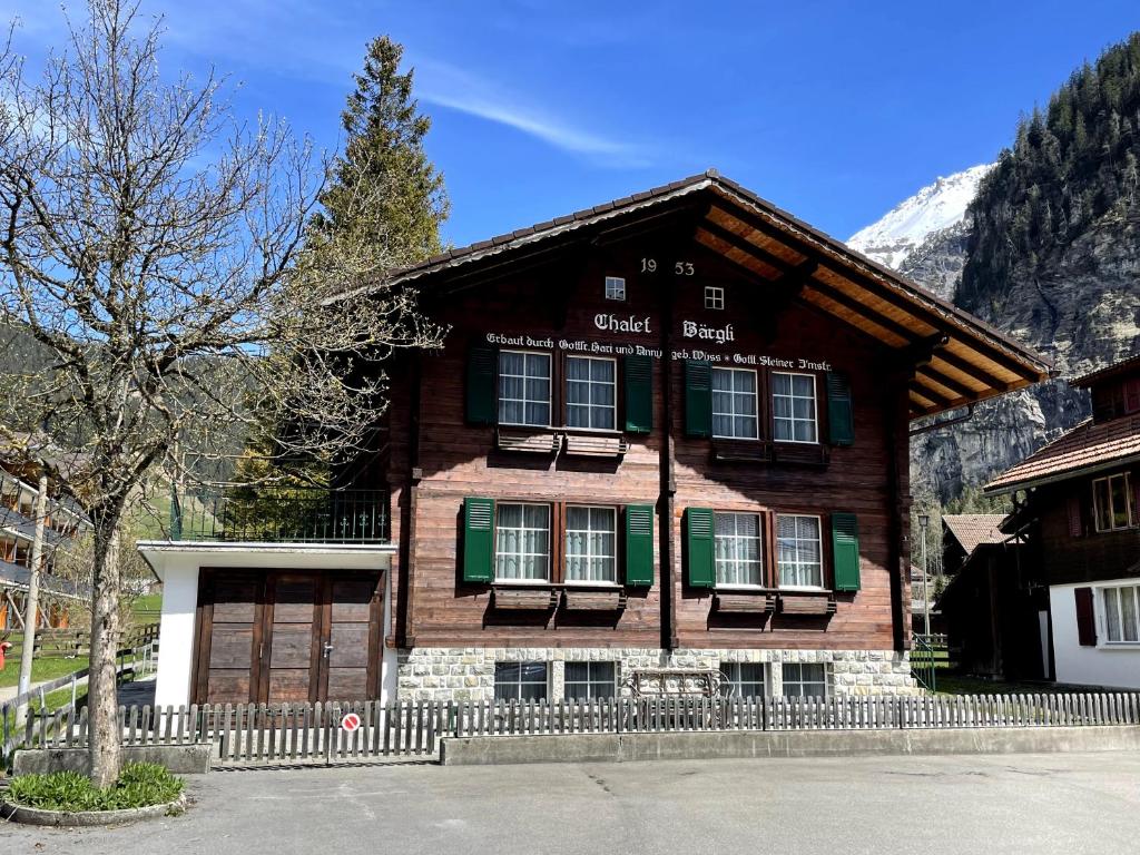 ein großes Holzhaus mit einem Zaun davor in der Unterkunft Familienferien im Chalet Bärgli Kandersteg in Kandersteg